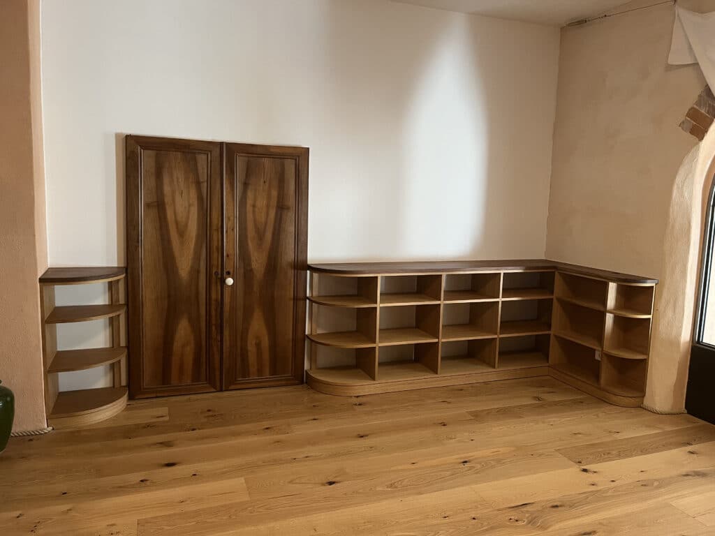 Meubles en bois sur mesure : placard noyer et étagère d'angle. Intérieur rénové : sol bois clair, grand placard noyer, étagères d'angle modulaires en chêne clair sur mesure avec bords arrondis.